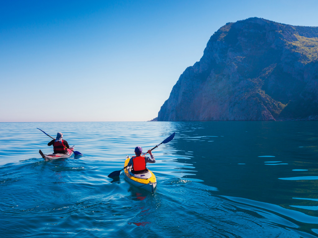 two people kayaking on asea with mountain