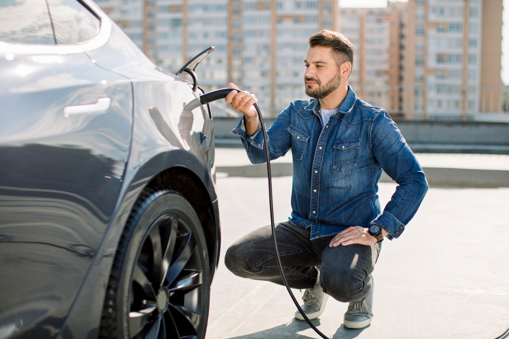 A car owner squats to plug in the cable of a charging station into their electric vehicle